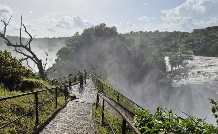 Visitors standing on a paved lookout trail surrounded by mist near the dramatic, rushing waters at the top of Murchison Falls.
