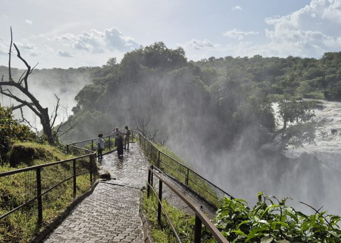 Visitors standing on a paved lookout trail surrounded by mist near the dramatic, rushing waters at the top of Murchison Falls.